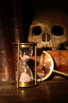 Vintage still life. Magnifying glass near hourglass on background with old book