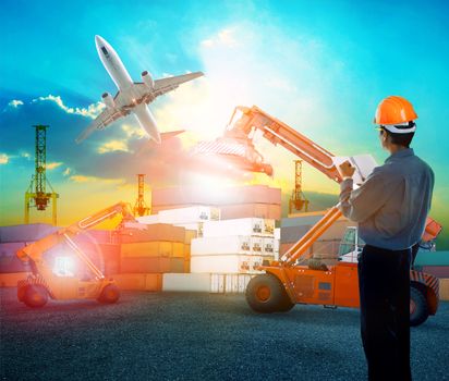 working man in logistic business working in container shipping yard with dusky sky and jet plane cargo flying above use for land to air transport and freight