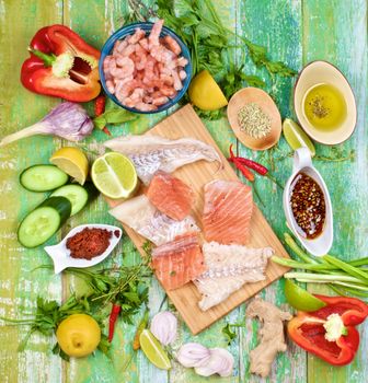 Raw Ingredients of Thai Fish Cakes with Vegetables, Spices, Herbs, Fruits, Prawns and Delicious Fillet of Salmon and Cod closeup on Cracked Wooden background. Top View