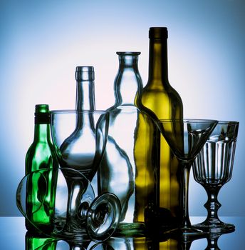Arrangement of Various Empty Wine, Martini and Cognac Glasses and Colored Empty Bottles with Reflection on Glass and Shadow Toned Backlight