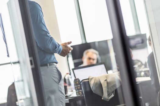Business man making a presentation at office. Business executive delivering a presentation to his colleagues during meeting or business training. View through glass. Business and entrepreneurship.