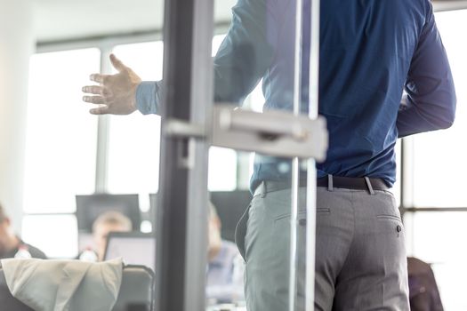 Business man making a presentation at office. Business executive delivering a presentation to his colleagues during meeting or business training. View through glass. Business and entrepreneurship.