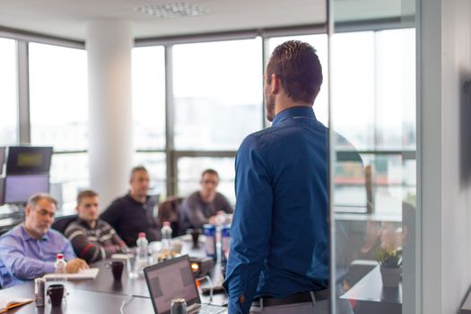 Business man making a presentation at office. Business executive delivering a presentation to his colleagues during meeting or in-house business training. Rear view. Business and entrepreneurship.