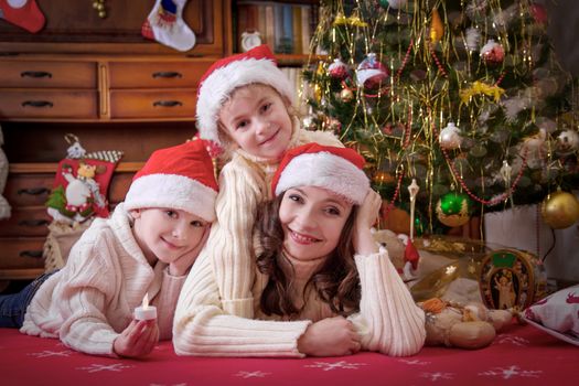 Smiling mother and two children lying under Christmas tree