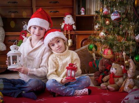 Two children with lanterns sitting under Christmas tree