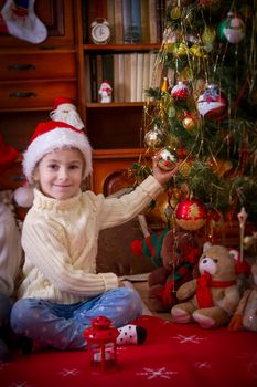 Smiling girl sitting under Christmas tree holding ball