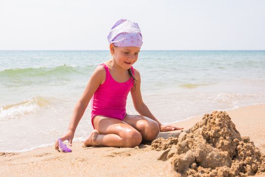 Girl happily looks at the sand pit dug up, sitting on the beach