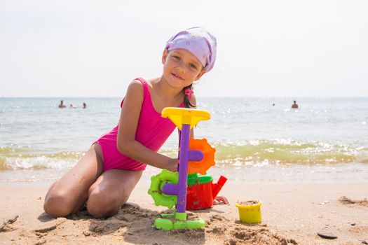 The girl in pink swimsuit playing with sand toys on the beach