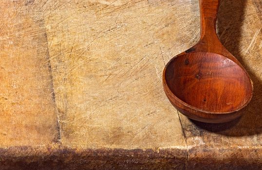 Empty wooden spoon lying on a rough wooden background. Rural style still live close up image with copyspace.