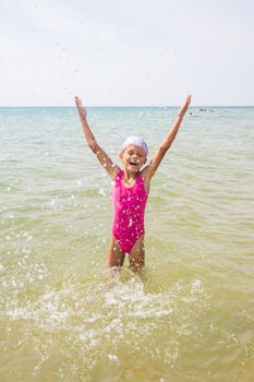 Happy girl let up splashes water standing in sea