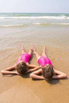 Two girls lie on your back on the sandy beach halfway in the wate