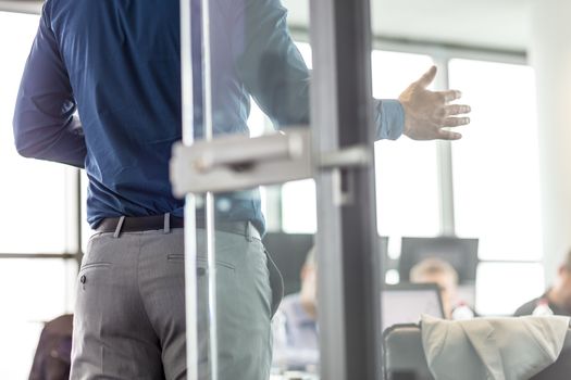 Business man making a presentation at office. Business executive delivering a presentation to his colleagues during meeting or business training. View through glass. Business and entrepreneurship.