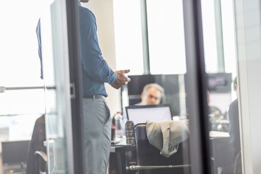 Business man making a presentation at office. Business executive delivering a presentation to his colleagues during meeting or business training. View through glass. Business and entrepreneurship.