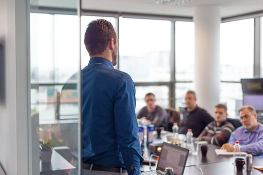 Business man making a presentation at office. Business executive delivering a presentation to his colleagues during meeting or in-house business training. Rear view. Business and entrepreneurship.