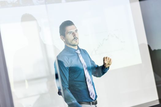 Business man making a presentation in front of whiteboard. Business executive delivering a presentation to his colleagues during meeting or in-house business training. View through glass.