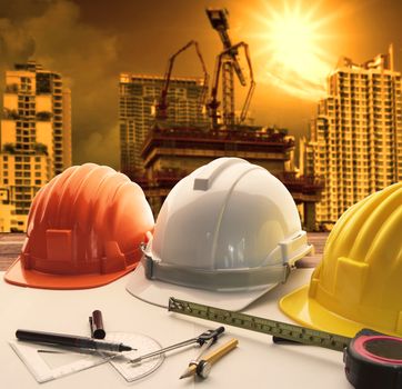 safety helmet on architect ,engineer working table with modern building and crane construction background use for construction business and civil engineering ,real estate topic