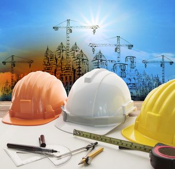 safety helmet on architect ,engineer working table with modern building and crane construction background use for construction business and civil engineering ,real estate topic