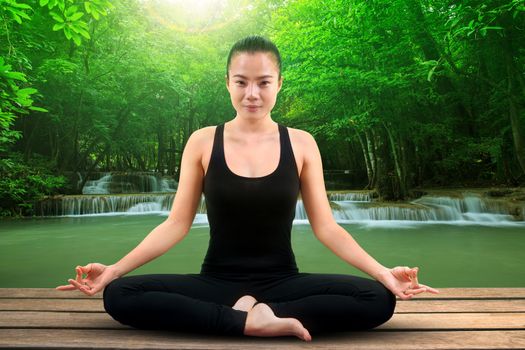 portrait of asian woman wearing black body suit sitting in yoga meditation position with beautiful natural scene of water falls