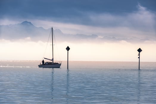 Landscape with a single boat sailing on the Bodensee lake  and the Alps mountains covered with mist at the horizon, in the morning light.