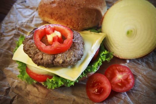 close up of ham cheese burger and bun with tomato onion and green vegetable on brown paper ready for meal eating