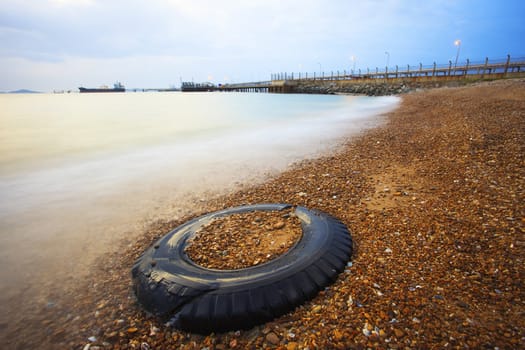 old truck tire on gravel beach against beautiful sea water with long explosure technical photography
