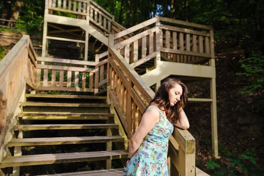 Brunette girl sitting on the wooden stairs in park and smiling