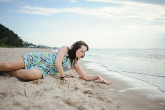 Young attractive brunette woman on a beach wearing dress
