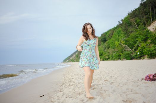 Young attractive brunette woman on a beach wearing dress