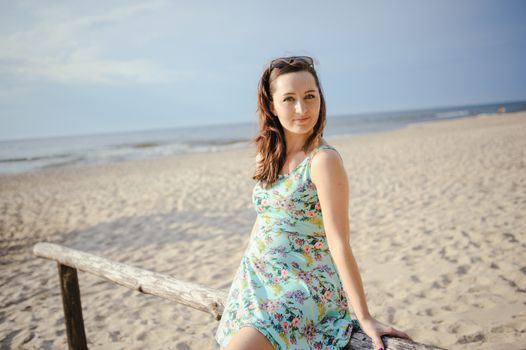 Young attractive brunette woman on a beach wearing dress