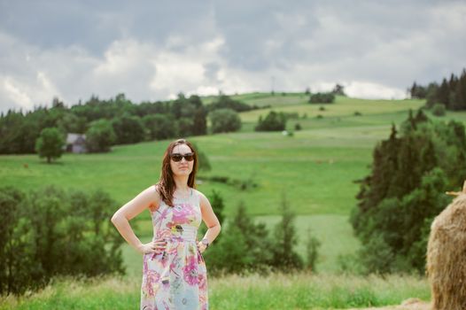 Brunette girl enjoying journey in mountains. Young smiling woman wearing dress traveling in countryside