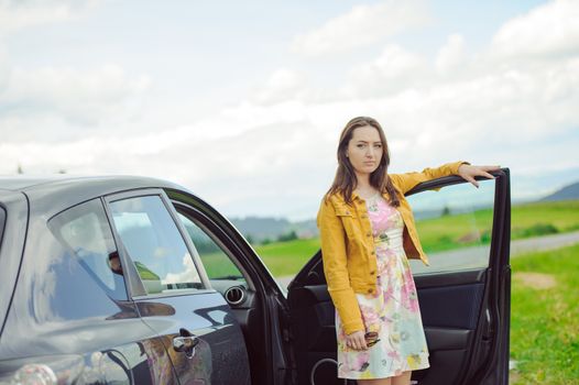 Young brunette girl standing next to the car with open door