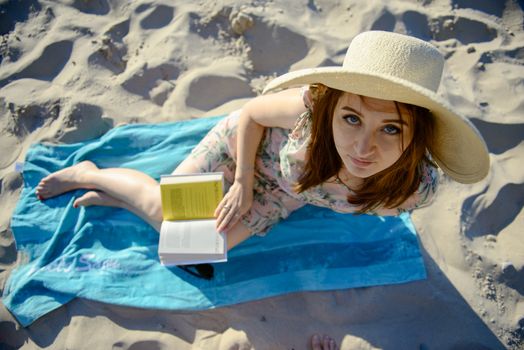 Portrait of a young brunette relaxing on the beach, reading a book. Summer time