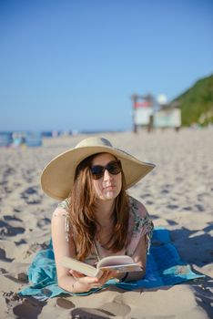 Portrait of a young brunette relaxing on the beach, reading a book. Summer time