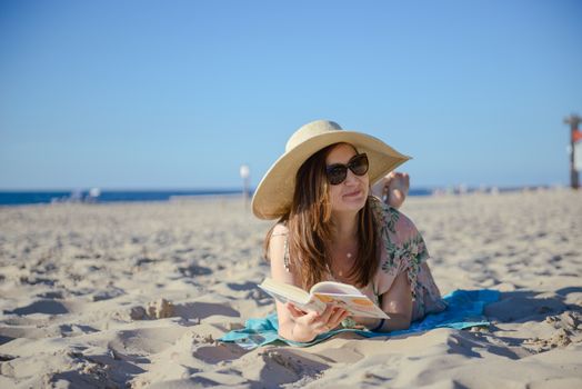 Portrait of a young brunette relaxing on the beach, reading a book. Summer time