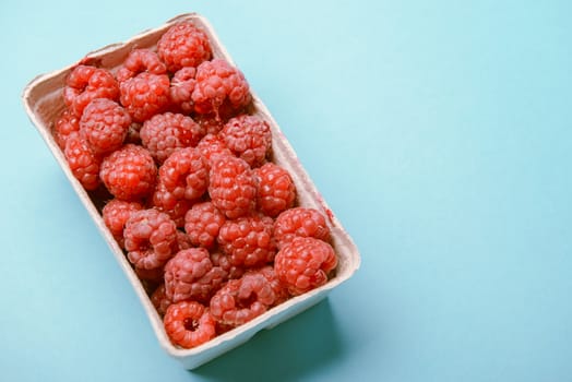 box of fresh raspberries on a blue background