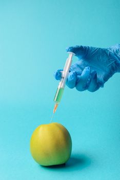 Chemical additives in food or genetically modified fruit concept. Green apple with syringes of chemicals. Isolated on blue background.