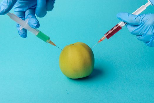 Chemical additives in food or genetically modified fruit concept. Green apple with syringes of chemicals. Isolated on blue background.