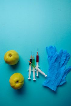 Chemical additives in food or genetically modified fruit concept. Green apple with syringes of chemicals. Isolated on blue background.