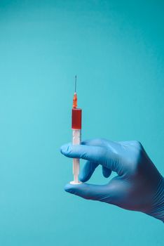 Hand in glove with syringe on blue background. Injections.