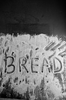Word bread written in flour on table.