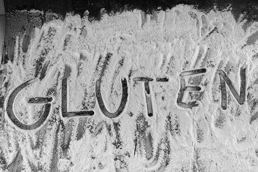 gluten word written in wheat flour on dark board.