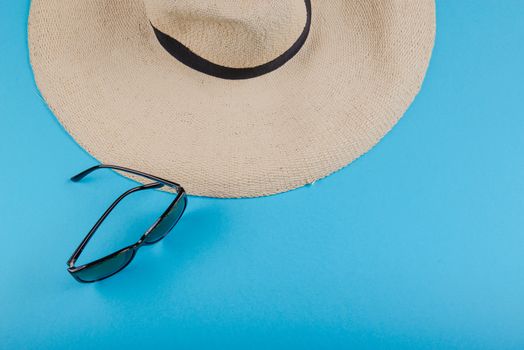 Straw hat and sunglasses on blue background. beach equipment.