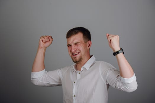 Young successful businessman standing with hands up and celebrating success. Gray background.