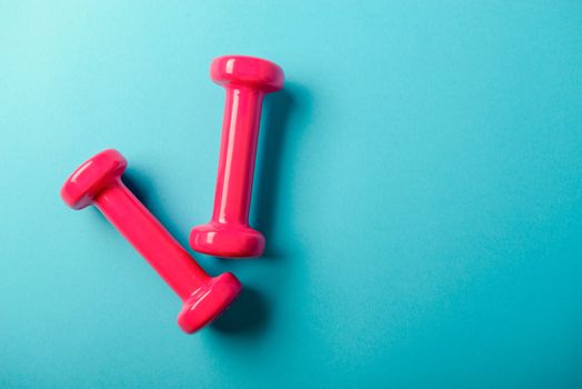 Pair of pink 1 kg dumbbells on blue background and water bottle