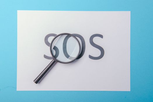 Word SOS written on white paper. Blue background