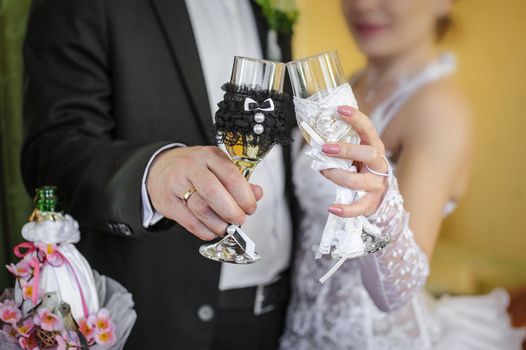 Beautiful decorated wedding glasses in the hands of the bride and groom