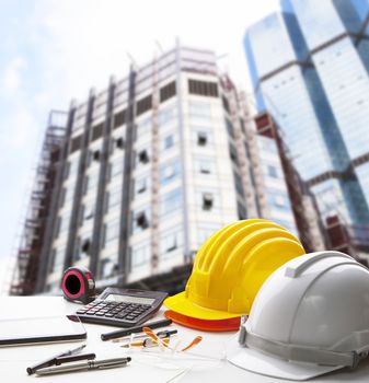 safety helmet and writing instrument on engineering working table against exterior construction building