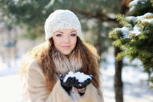 Young woman in hat and mittens laughing playing with snow outdoors. 