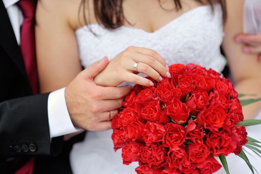 Hands of bride and groom with rings on wedding bouquet