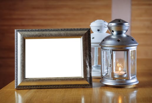 old photo frame on the wooden table against the background of a lantern with a candle